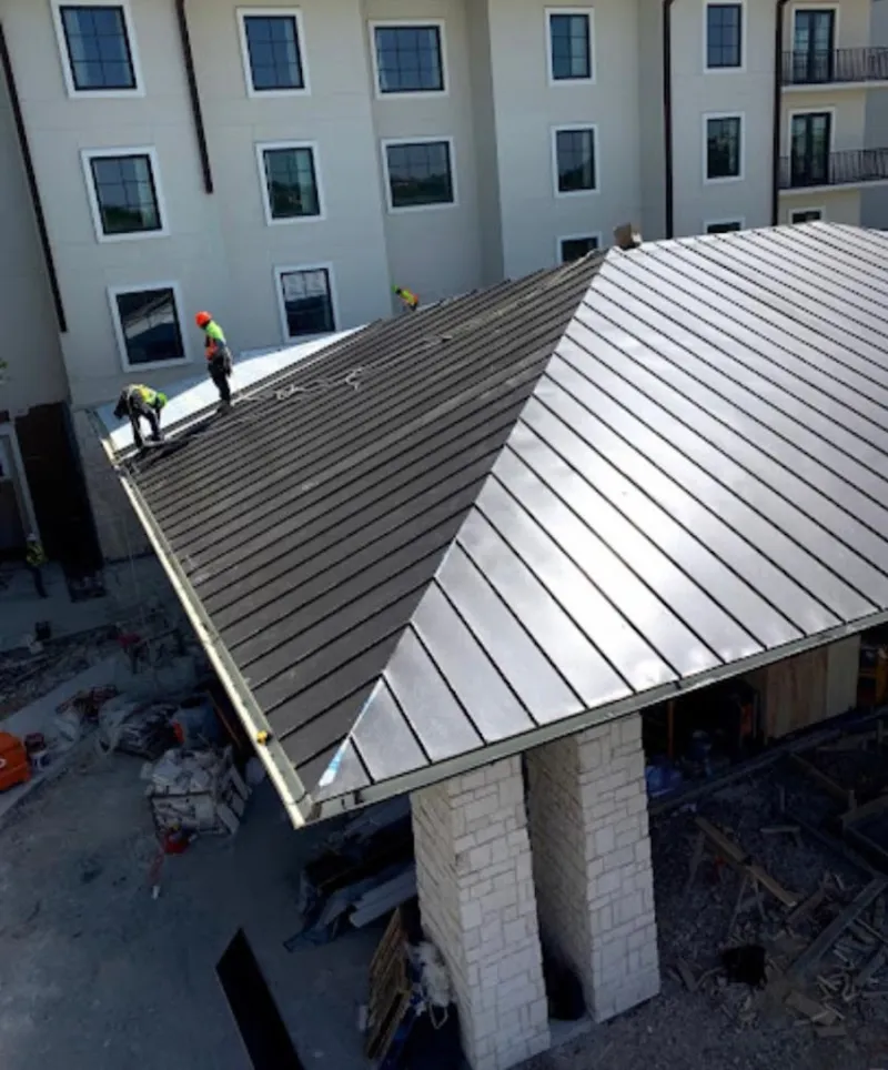 Crew installing standing seam metal roof panels on a commercial project in Pelham Manor